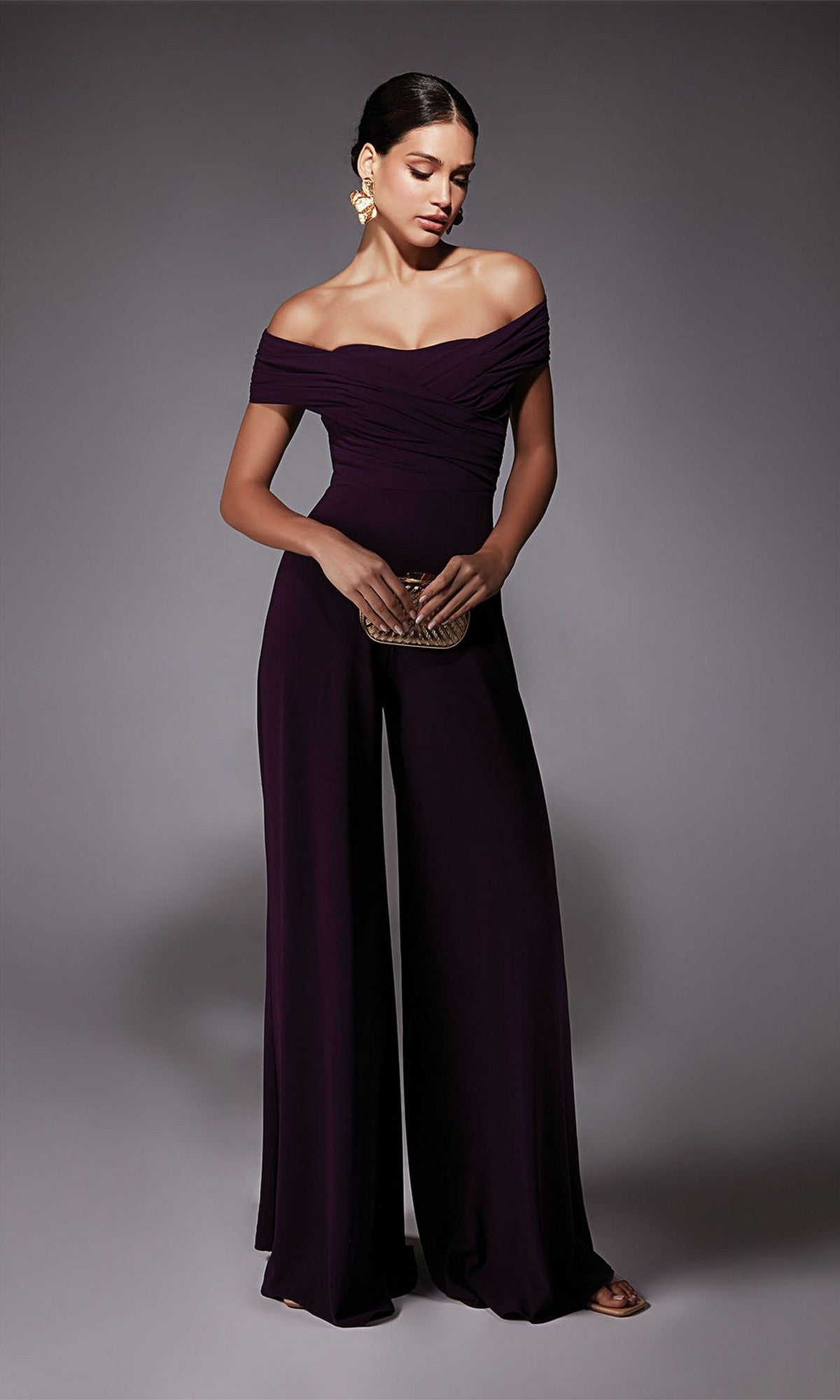 Woman wearing the Alyce 70067 long formal dress in eggplant, posing with a small clutch against a plain grey background.